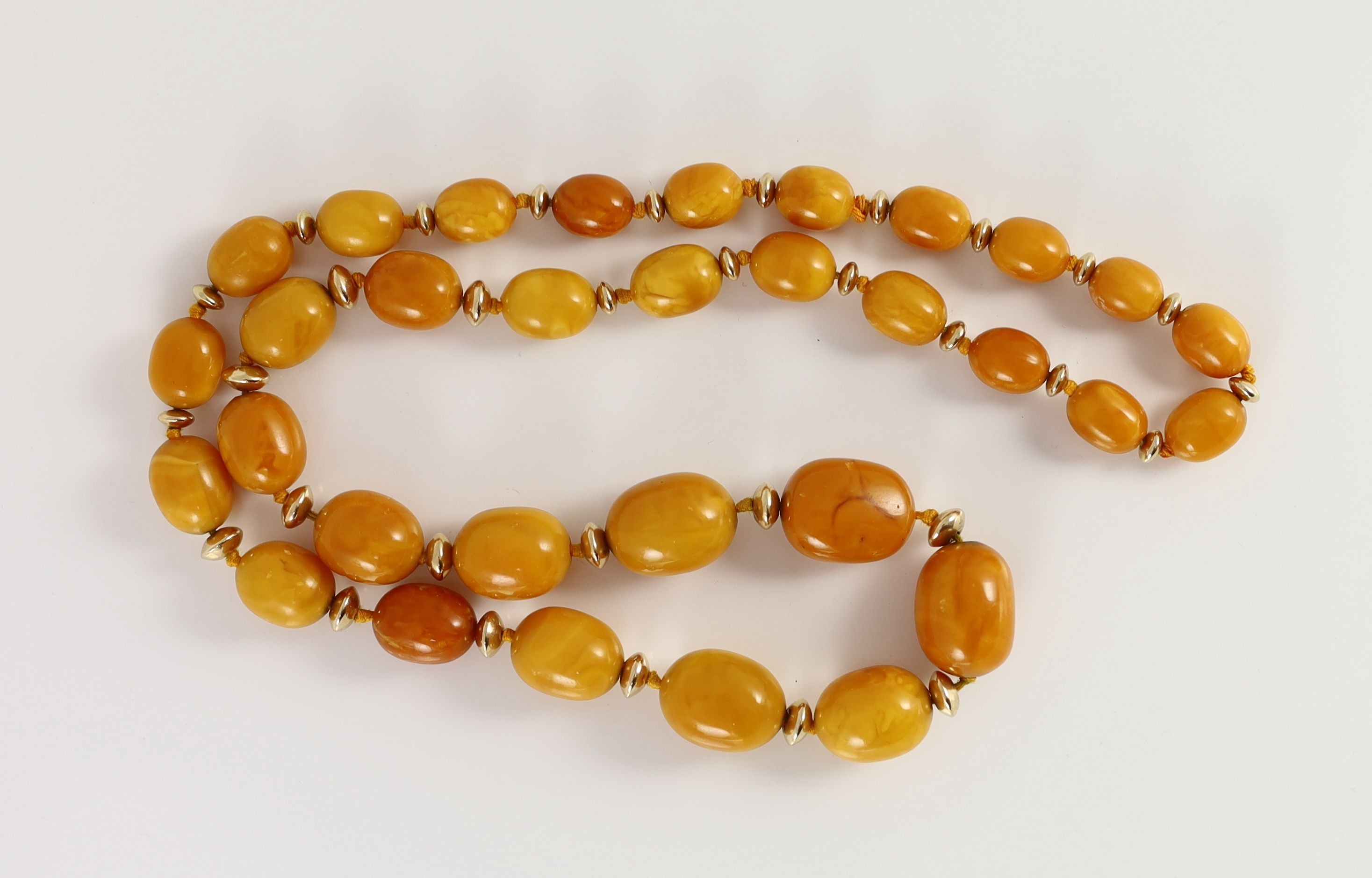 A single strand graduated oval amber bead necklace, with gilt metal spacers, 80cm, gross weight 92 grams.